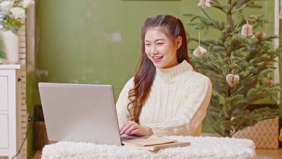 亚洲女商人工作呆在家里圣诞树在背景庆祝工作成功自由职业妇女在平安夜用电脑工作假期工作概念