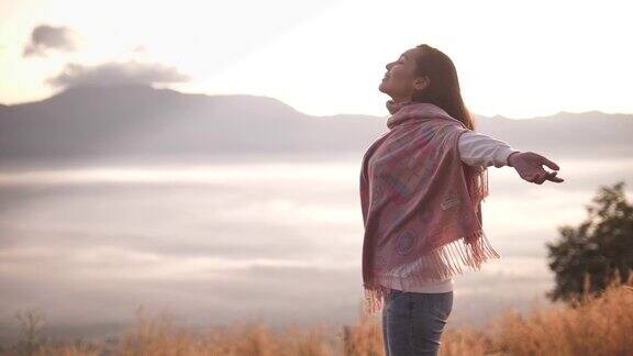 自由亚洲女人站在山顶张开双臂欣赏日落
