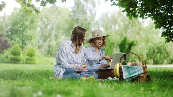 两个女人一边喝酒一边用笔记本电脑在野外野餐