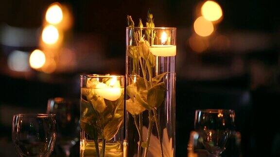 婚礼宴会厅的内部细节与装饰餐桌设置在餐厅蜡烛和白色花瓣装饰玫瑰花在玻璃花瓶装满水
