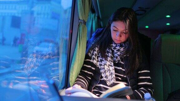 女乘客晚上乘公共汽车时看书晚上女孩在窗口旁边的一辆移动的车上读故事