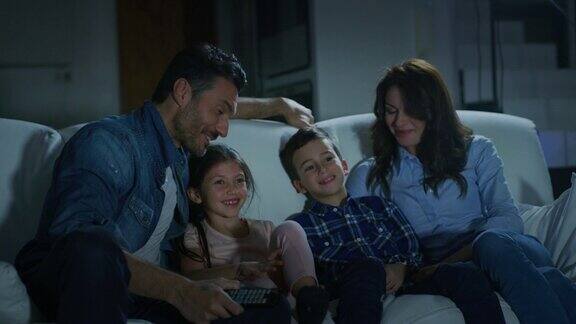 晚上在客厅沙发上看电视的幸福家庭的慢镜头