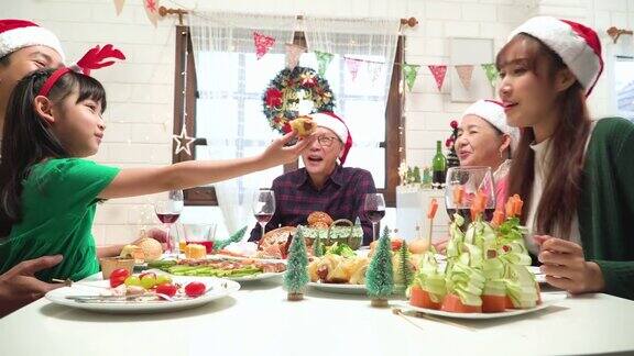 东南亚几代同堂的家庭围坐在一张可爱的餐桌上为圣诞晚餐和团聚在家里装饰着树和装饰品低角度观:十几岁的女儿喂给母亲健康的食物、面包和爱