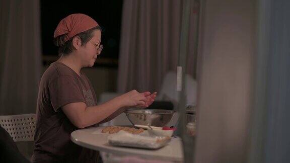 亚洲华人中成年妇女在家里的厨房里双手将花生饼干面团压在手掌上成型