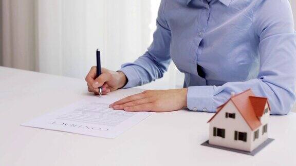女商人带着房子模型和钢笔在办公室签署合同文件