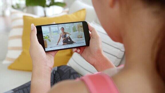 运动女性在家中智能手机屏幕上观看和学习运动锻炼在线瑜伽教练