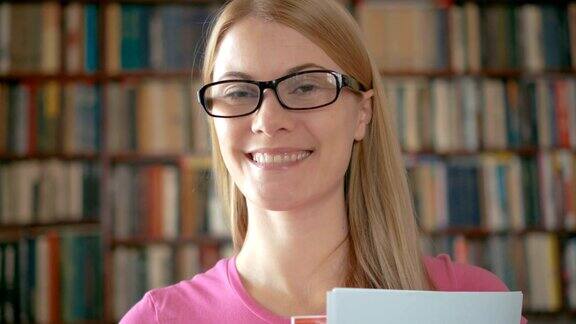 一个戴眼镜的兴高采烈的学生站在图书馆的肖像书架的背景