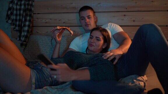 一对夫妻在床上看电视吃披萨
