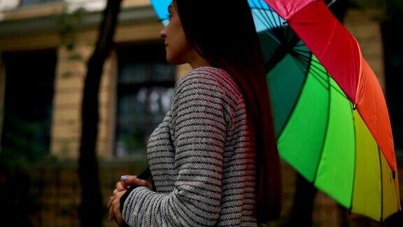 一个年轻美丽的女人在雨天在城市街道上行走和旋转她的彩色雨伞的特写视图Slowmotion拍摄
