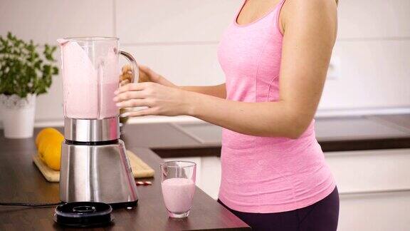 运动的年轻女子在厨房里喝草莓奶昔