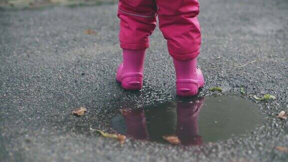 快乐的小女孩跑过水坑特写可爱的小女孩在雨后穿着粉红色的胶靴走路