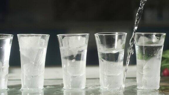 酒保把伏特加从瓶子里倒进几个冰玻璃杯里
