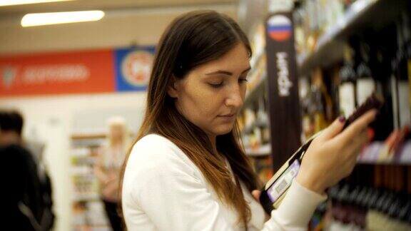 一个穿着便服的女孩在超市挑选葡萄酒拿着店里架子上的一瓶酒侧视图