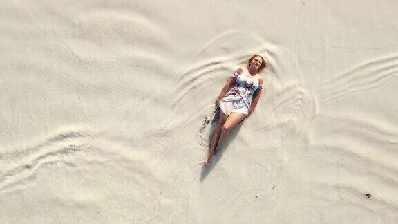 一个快乐的女人穿着太阳裙躺在沙滩上