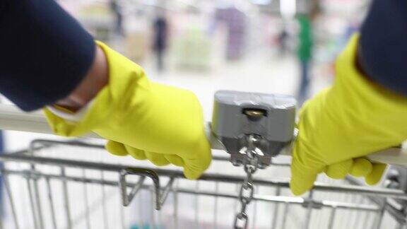 在商店里戴着橡胶手套的男人的手拿着购物车