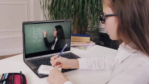 远程教育在线教育女学生在笔记本电脑屏幕上观看在线教程视频并在笔记本上做笔记在家在线学习