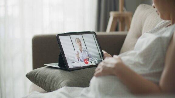 亚洲孕妇在家用数码平板电脑与医生视频通话