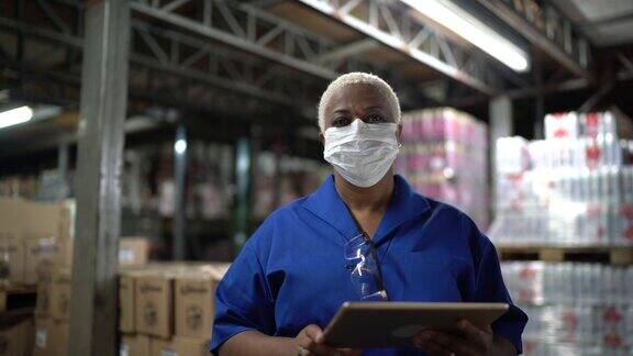 在仓库工业中工作的妇女戴着面具使用数字平板电脑的肖像