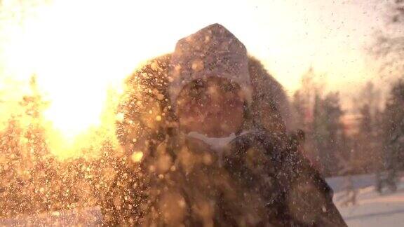 慢镜头:在神奇的冬天年轻女子在夕阳下吹着雪花