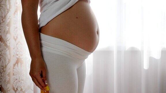 穿着白色衣服的孕妇在靠近窗户的地方用卷尺量大肚子