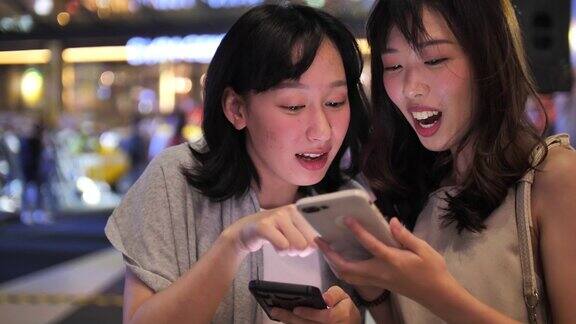 两个亚洲女人在晚上使用智能手机在智能手机上分享一些东西