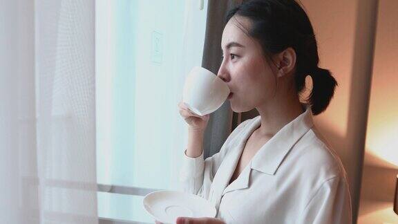 亚洲女人喝着早茶看着窗外她微笑着享受着阳光明媚的日子