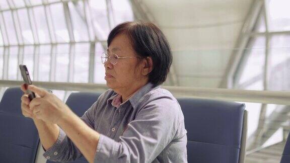 亚洲资深女乘客在候机楼用智能手机等待她的航班