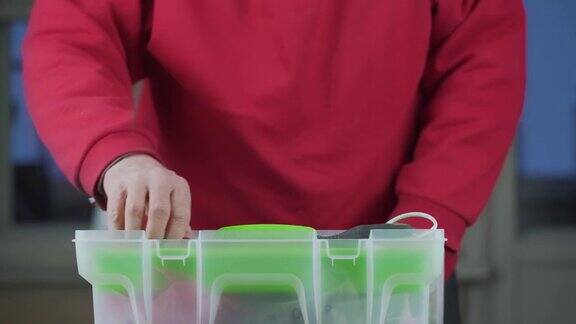 穿红套头衫的老修理工把塑料工具箱放在桌子上
