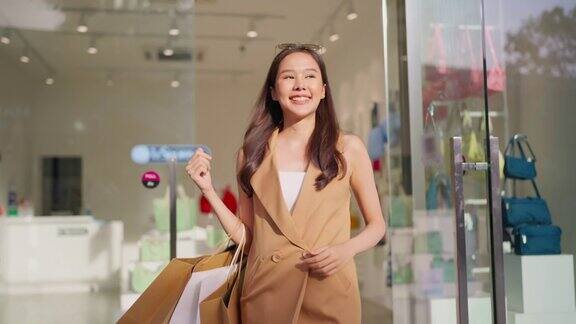 年轻的幸福美丽的亚洲女人拿着五颜六色的购物袋同时打开购物中心的玻璃大门店前女人离开商店与购物袋