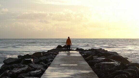 意大利莱万托一名男子站在码头上望着大海身穿黄色夹克夕阳西下