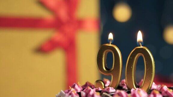 90号生日蛋糕用金色蜡烛点燃蓝色背景的礼物用黄色礼盒系上红丝带特写和慢动作