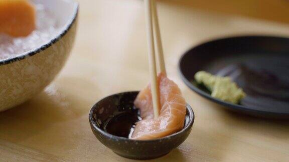 用筷子夹紧手挑三文鱼生鱼片在日本餐馆里蘸着大豆和芥末