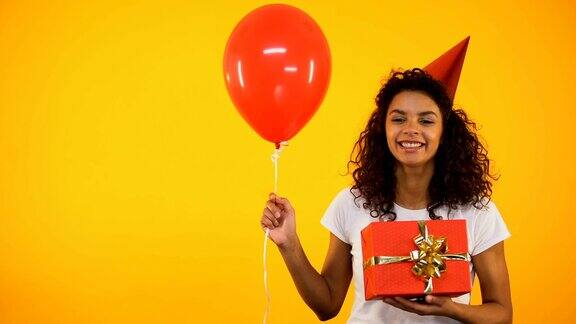 快乐的混血女孩拿着礼物盒和气球庆祝生日派对