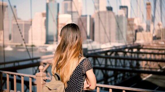 年轻的白人女性游客戴着时尚的太阳镜背包独自站在布鲁克林大桥纽约市4K