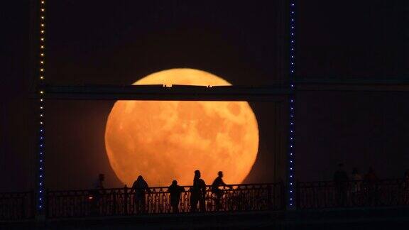 在升起的满月的背景下桥上人影的剪影