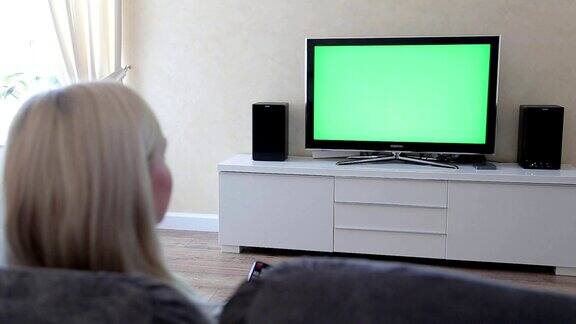 一个女人在绿屏幕上使用电视遥控器年轻女子看电视用绿色的屏幕拍摄背后的模特肩膀