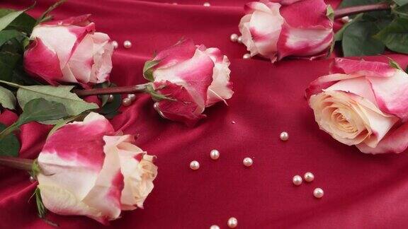 粉红色的珍珠落在深红色的缎子和粉红色的玫瑰上