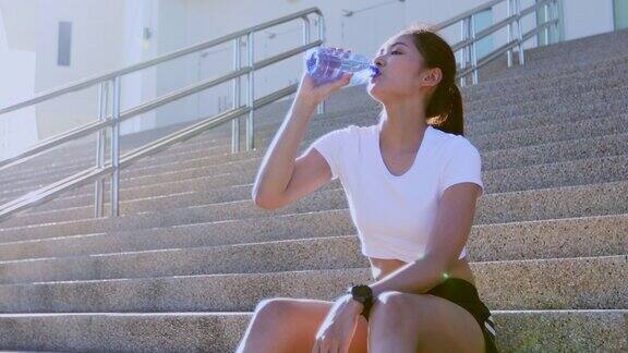 运动女子亚洲饮水后在阳光和她休息累了户外跑步