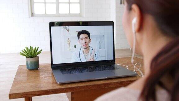 亚洲妇女与医生通过电脑笔记本电脑虚拟视频电话或视频会议在家里远程保健和远程医疗