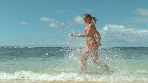 慢动作:顽皮的年轻白人女子在粉红色泳衣在海水中奔跑
