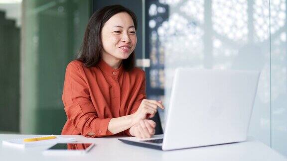 快乐友好的亚洲妇女在视频通话而坐在工作场所在现代办公室