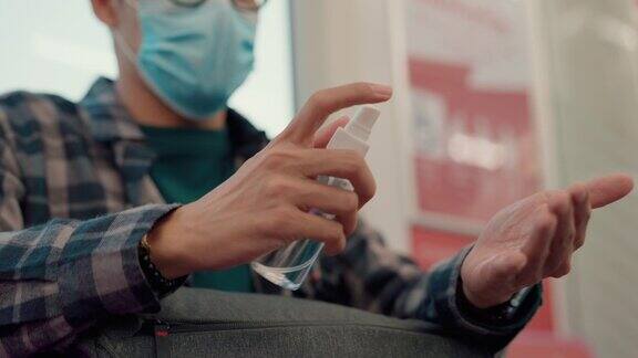 亚洲男子在冠状病毒疫情期间带口罩在公共交通工具上喷洒洗手液