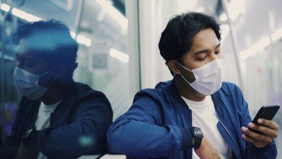 在冠状病毒爆发期间一名男子戴着防护口罩乘坐地铁并使用手机