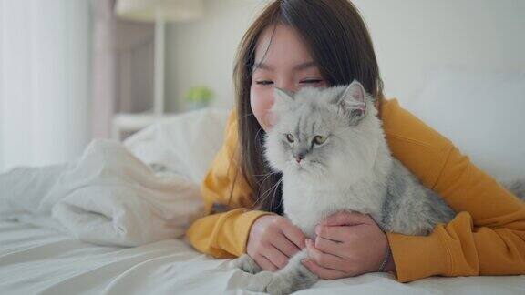 快乐的亚洲女人抱着毛茸茸的灰猫放松地躺在家里的床上宠物和主人之间的感人时刻宠物的友谊