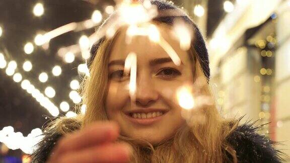 一个快乐的漂亮女人的肖像手里拿着闪闪发光的东西火花向不同的方向散射