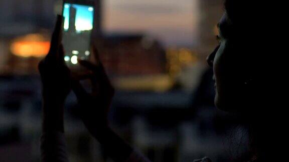 特写女人在酒吧屋顶露台上用智能手机拍摄城市风景的慢镜头