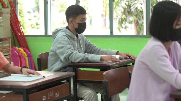 年轻老师用体温计检查亚洲小学生戴口罩防止病毒在进入教室前再次开始上课