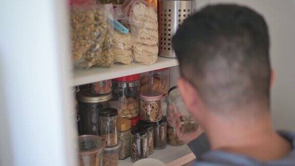 高角度观察亚洲华人男性从厨房的架子柜中取出食物瓶子