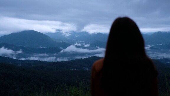 一个女旅行者的后视图看一个美丽的山脉等待日出在雾天