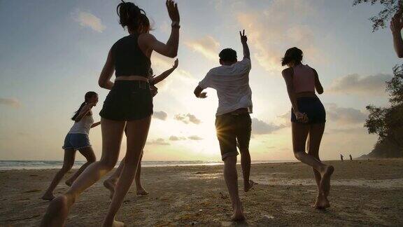 慢镜头-日落时分一群朋友在海滩上奔跑心情愉快有聚会庆祝观念的人后视图